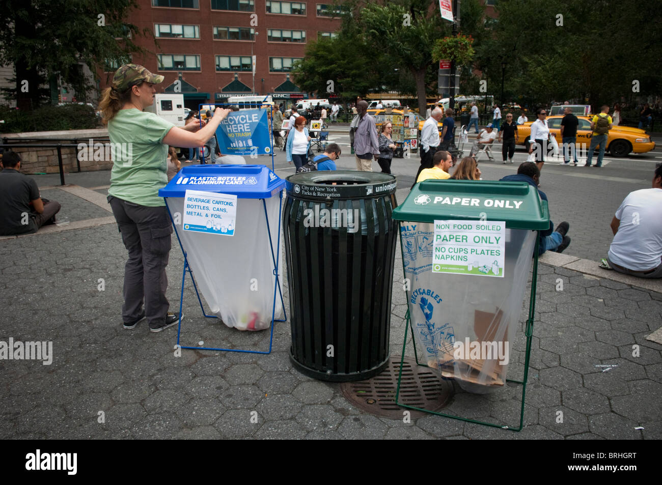 A woman adjusts a recycle here sign for a plastic bottles and aluminium cans bin in Union Square Park in New York Stock Photo