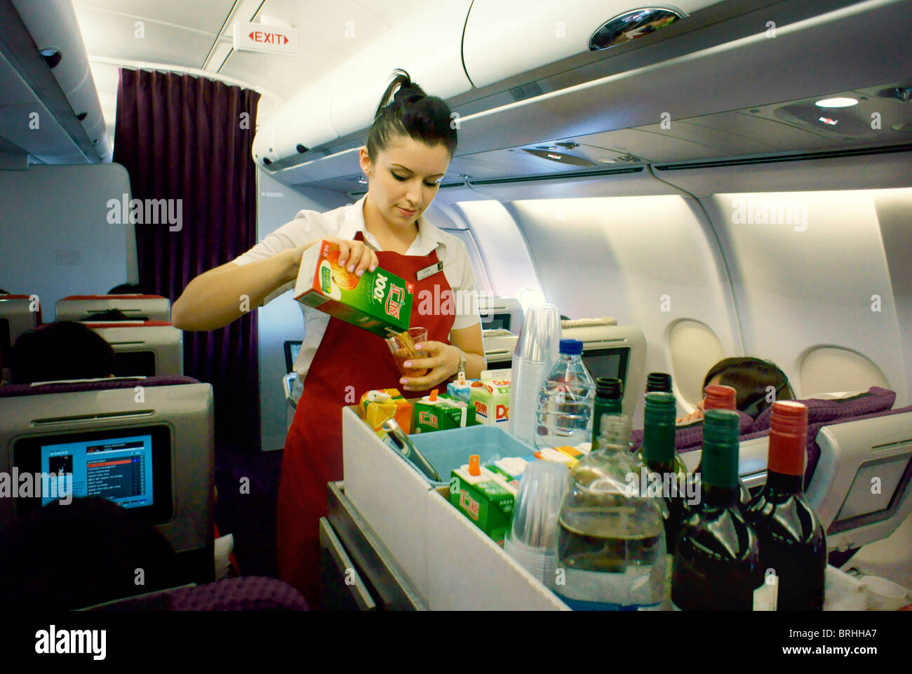 Long haul flight air stewardess with food drinks aisle trolley on overnight Virgin Atlantic aircraft serving drink to passenger Stock Photo