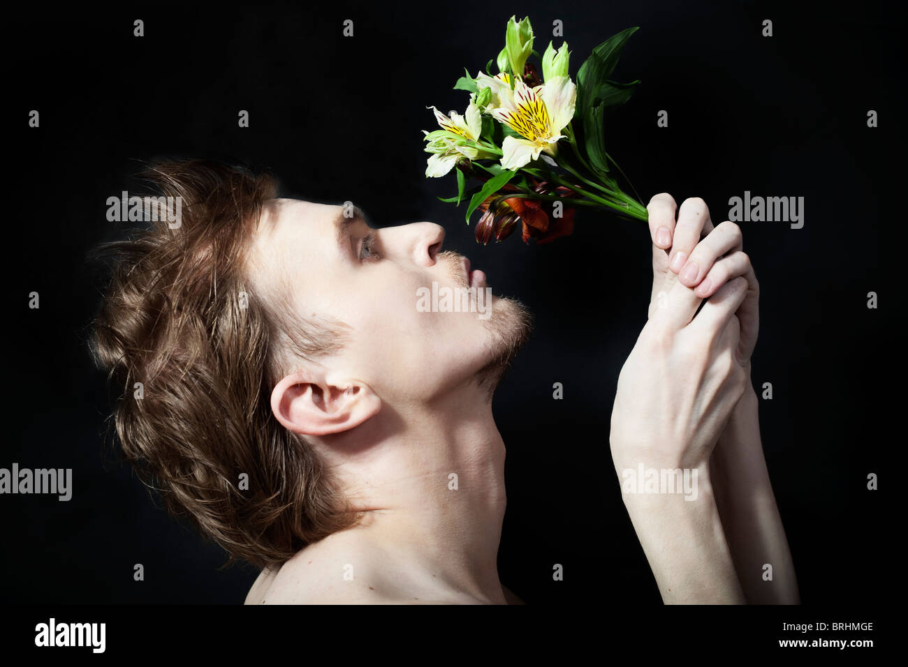 face of the young men sniffing bouquet of flowers on a black background Stock Photo