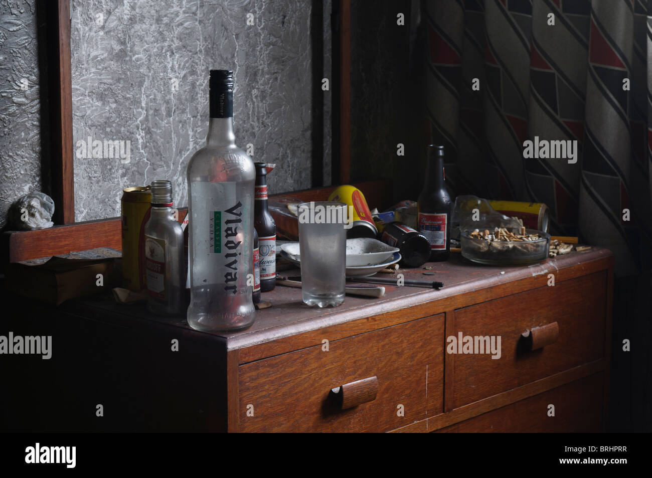 Very dirty bedside table with beer bottles, tins, vodka bottle and