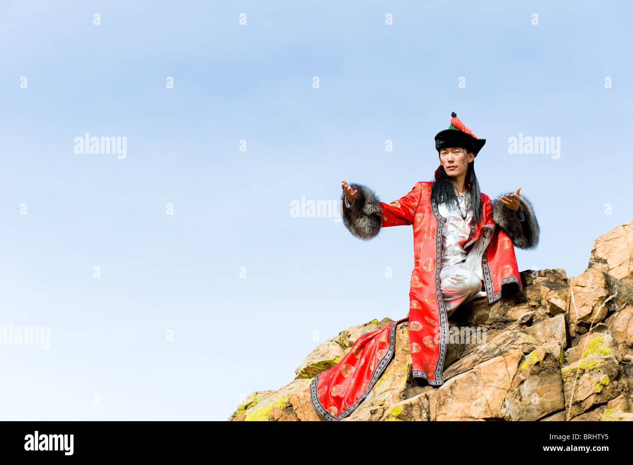 young asian man in fine Mongolian suit sits on rock Stock Photo