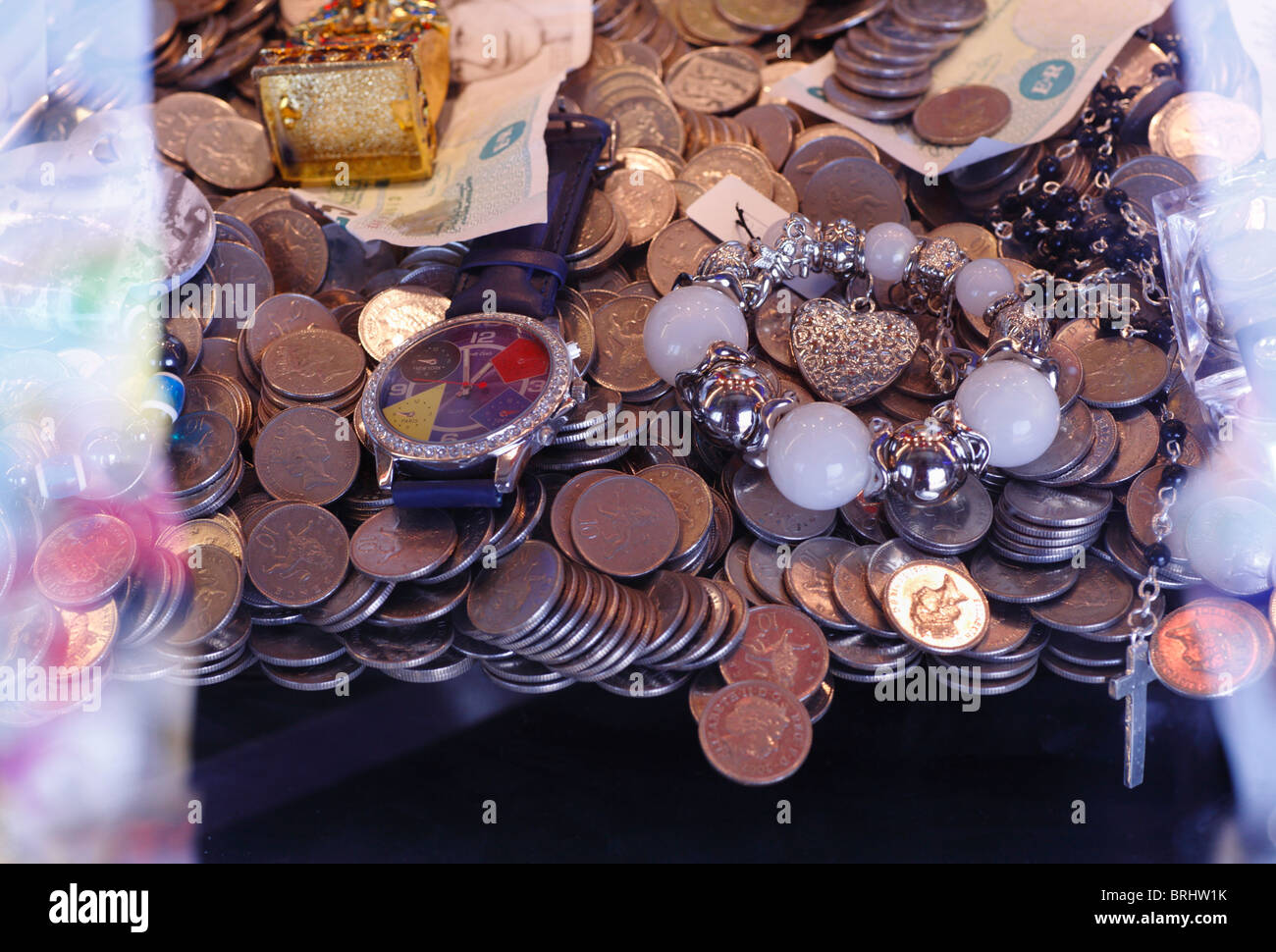Trinkets and coins in a penny falls at the funfair. Stock Photo