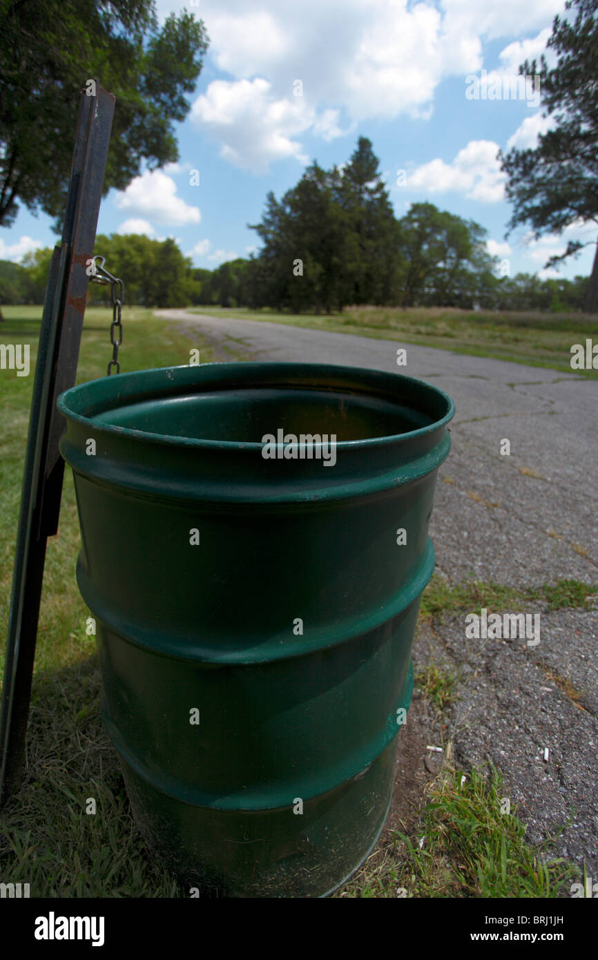 A trash can (rubbish barrel) next to a blacktop road in a public park. Stock Photo