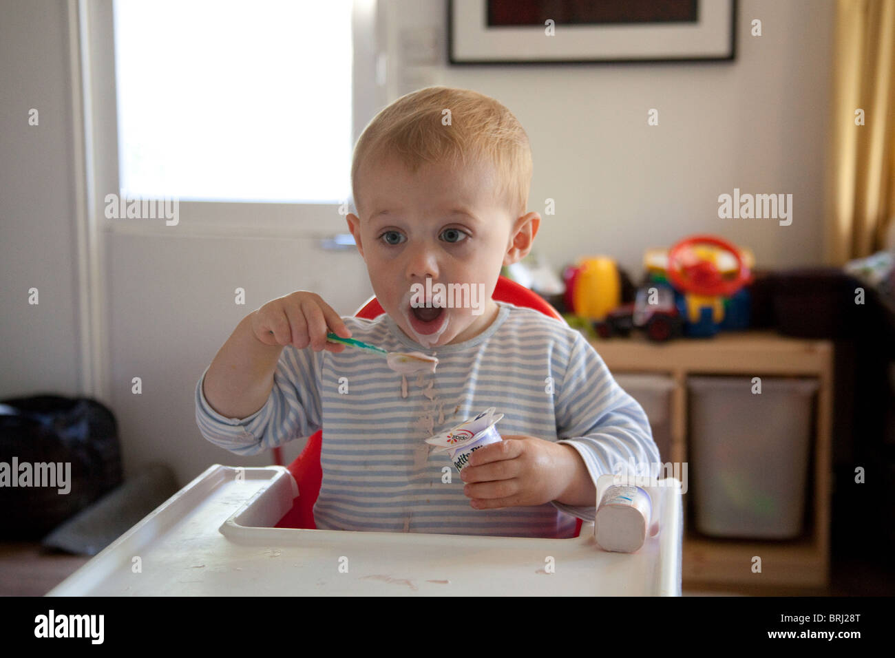 Young boy 16 months old eating a messily eating yogurt. Hampshire, England. Stock Photo