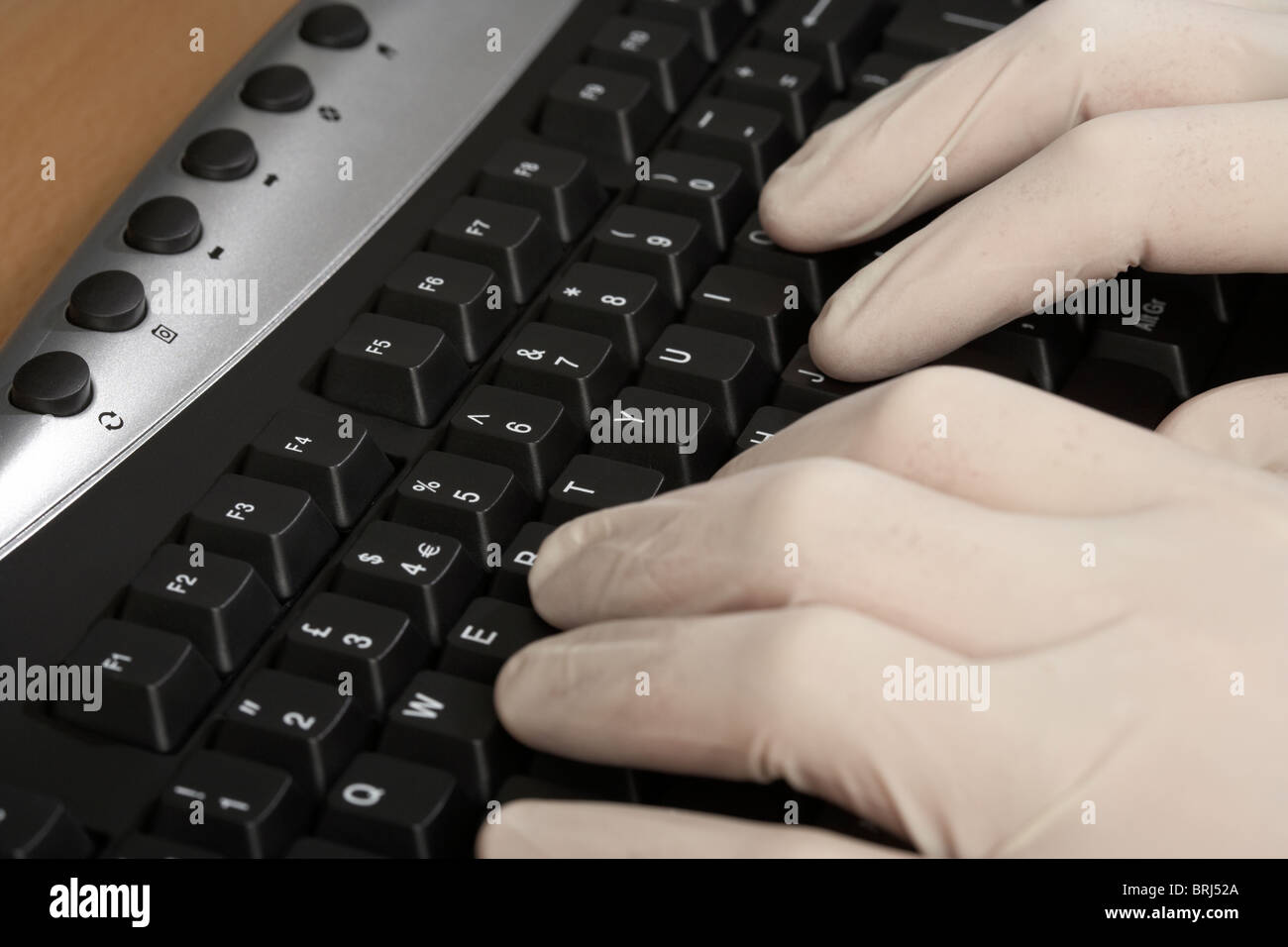 hands wearing surgical rubber white gloves typing at a computer keyboard Stock Photo