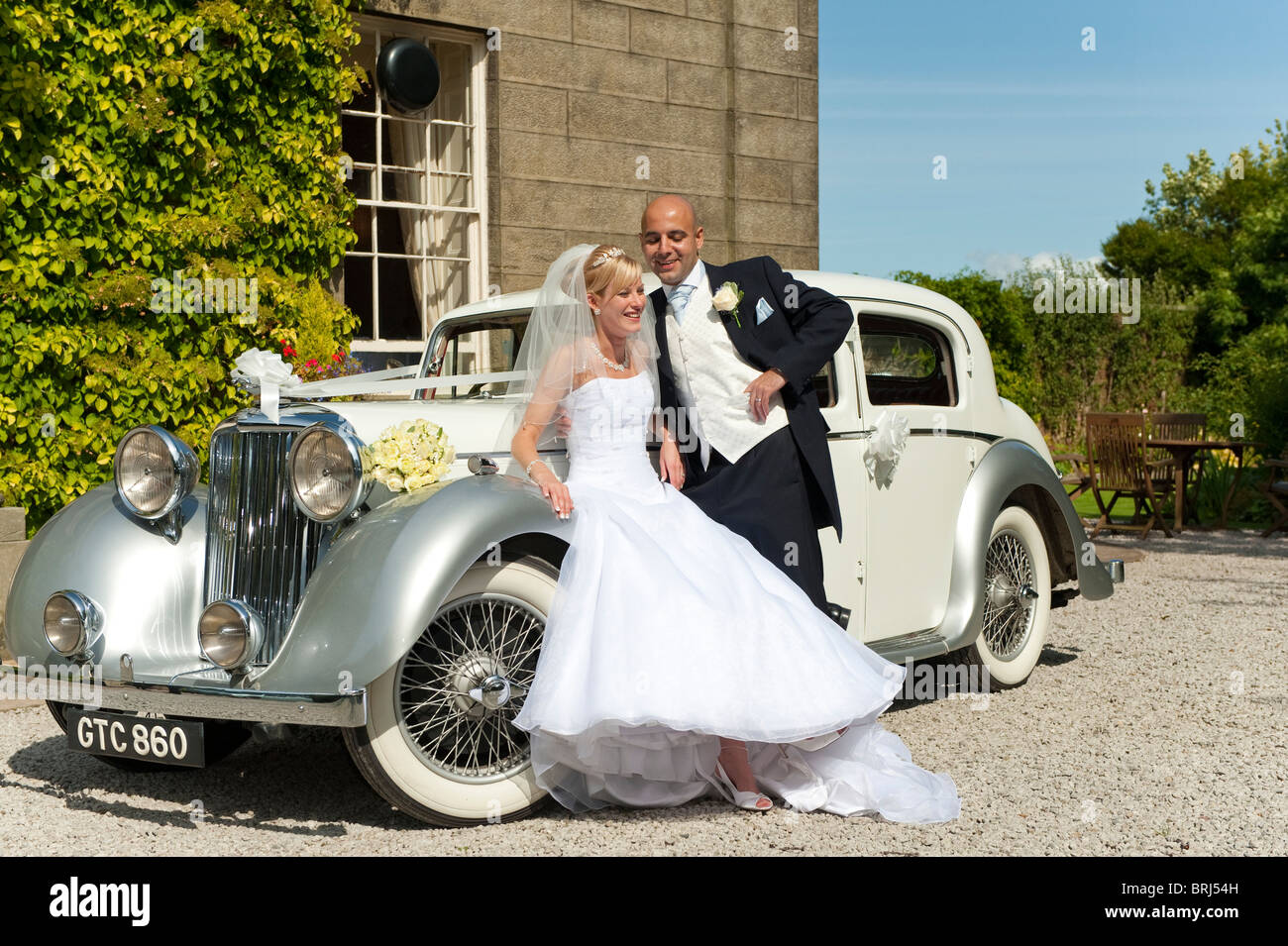 A stunning looking bride and groom next to a vintage wedding car Stock ...