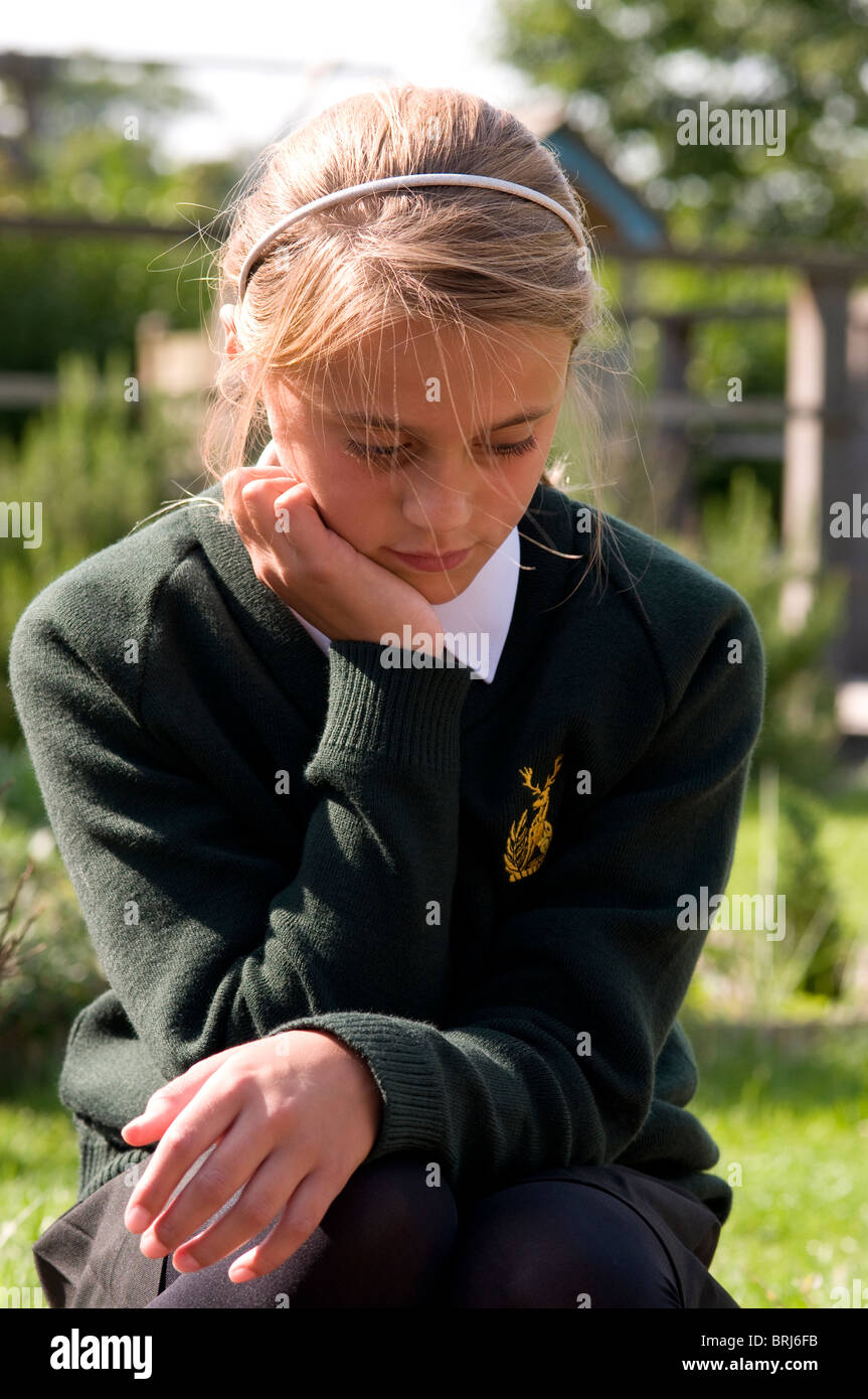 Schoolgirl with head leaning on her hand looking down and fed up Stock