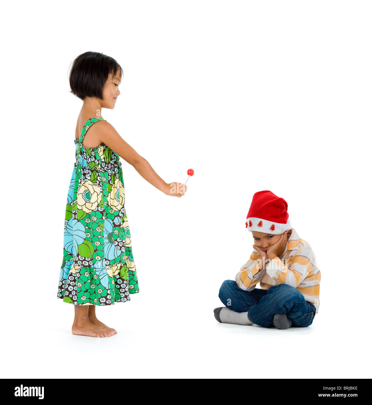 a little girl giving her friend a lollipop for christmas. they boy doesn't appreciate it at all. isolate on white background. Stock Photo