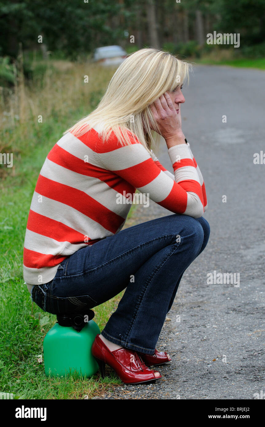 Woman motorist sitting on a fuel can at the roadside Stock Photo