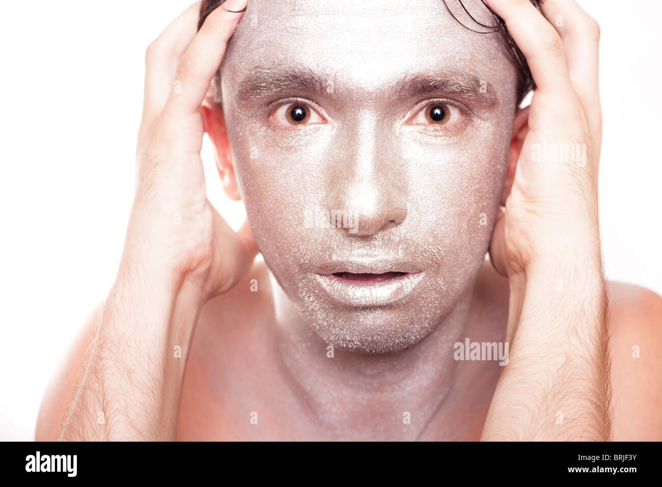 face of young man with frightened eyes and bronzed makeup close up Stock Photo