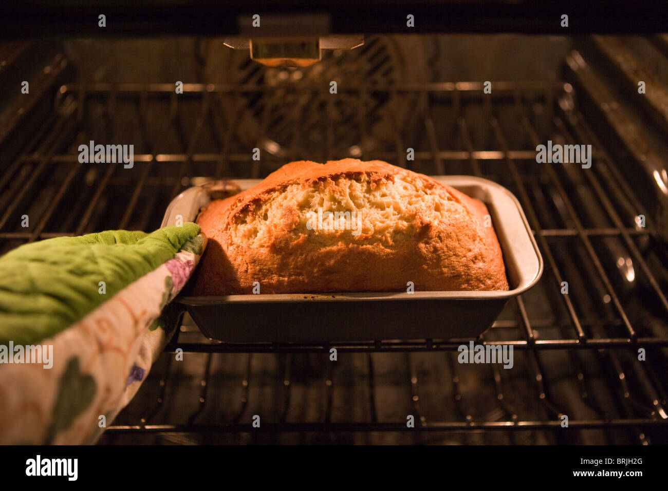 hand with oven mitt pulling out a loaf of home made banana bread from a hot oven Stock Photo