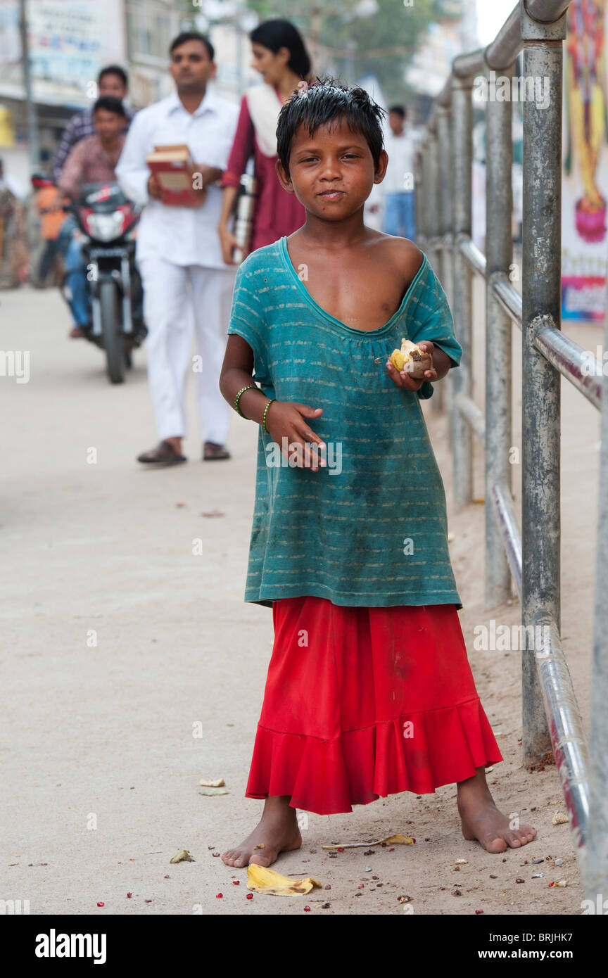 Young poor Indian beggar girl standing on the side of an indian street eating fruit. India Stock Photo