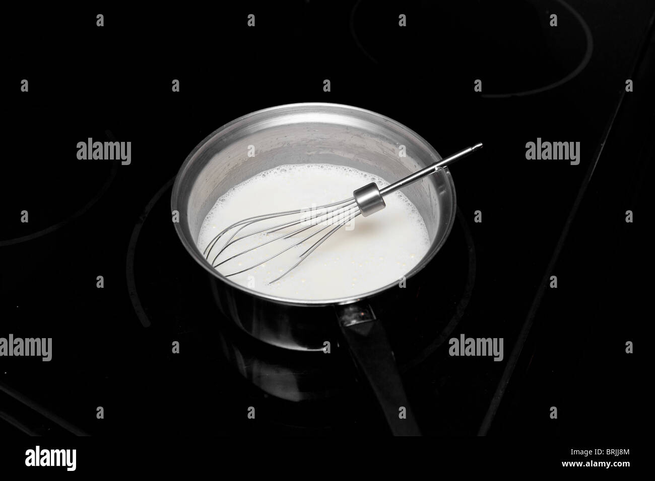 metal whisk in a small metal pan with heavy cream being stirred Stock