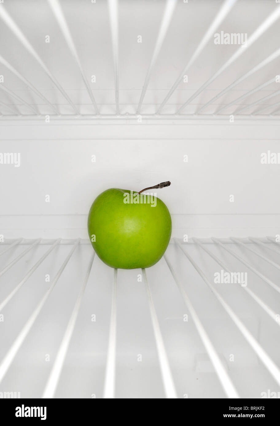 Single green apple sitting on shelf inside refrigerator Stock Photo