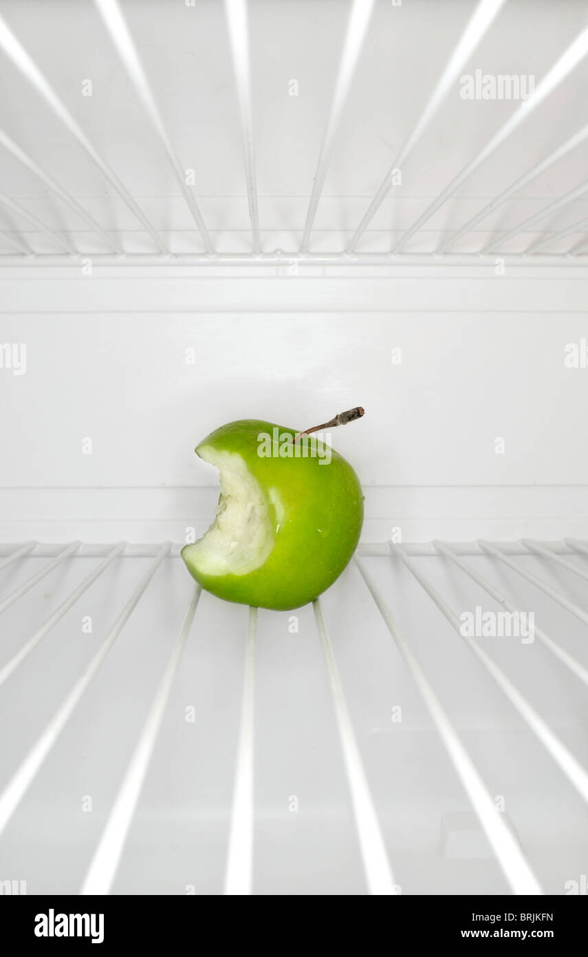 Single apple with bite mark sitting on shelf inside refrigerator Stock Photo