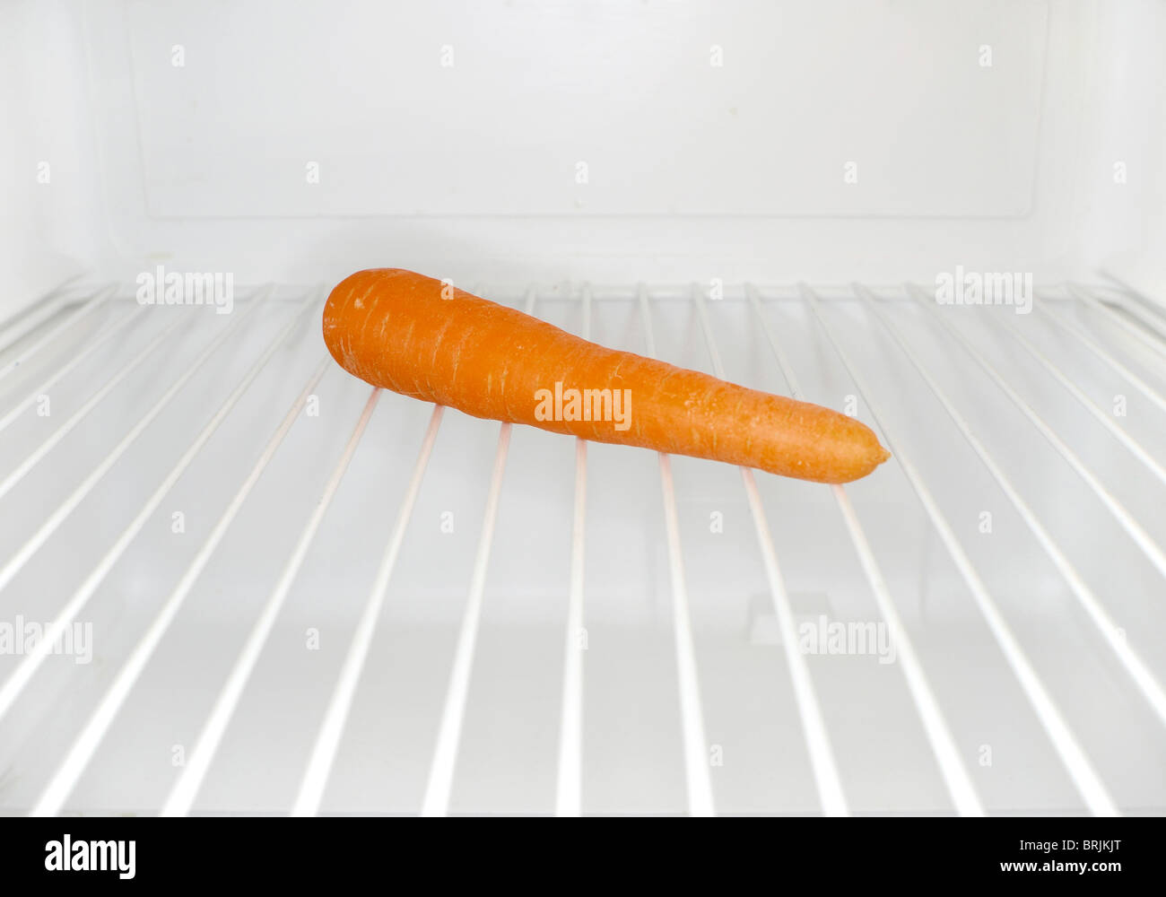 Single carrot sitting on shelf inside refrigerator Stock Photo