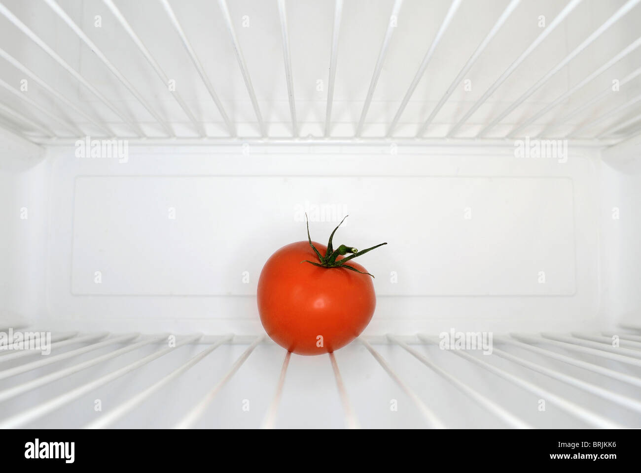 Single red tomato sitting on shelf inside refrigerator Stock Photo