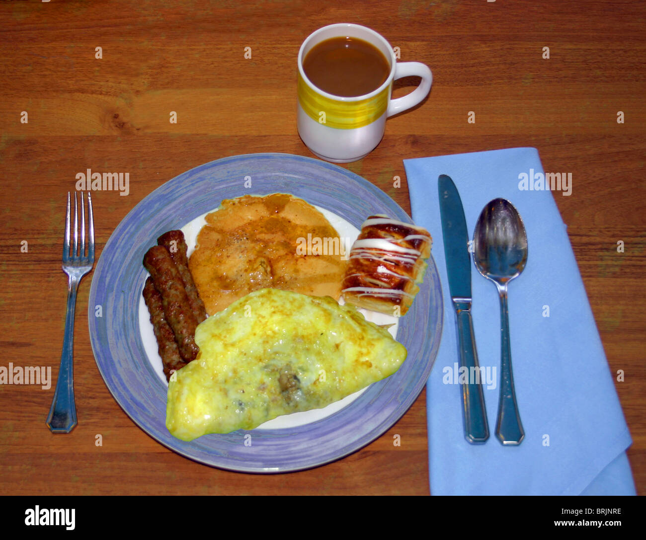 Morning breakfast meal with sausage, egg omelet, pancake, small sweet roll, and a cup of coffee.  All with blue and white plate. Stock Photo