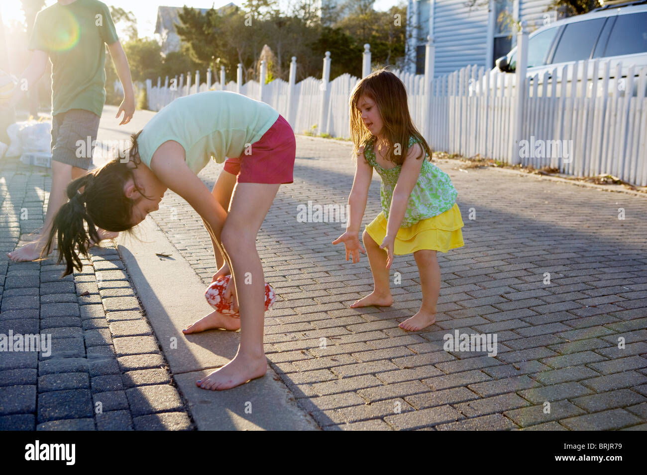 Two little girls are playing football in an alleyway with the sun in background. Stock Photo