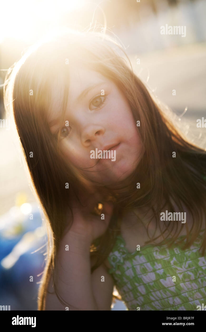 A little girl with long hair is staring at the camera with the sun shining through her hair. Stock Photo