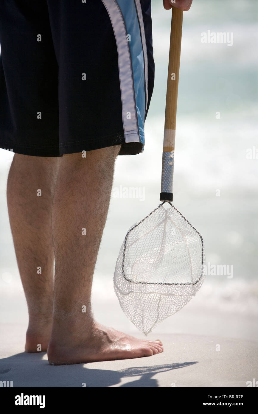 A man holds onto a bait net at the shoreline. Stock Photo