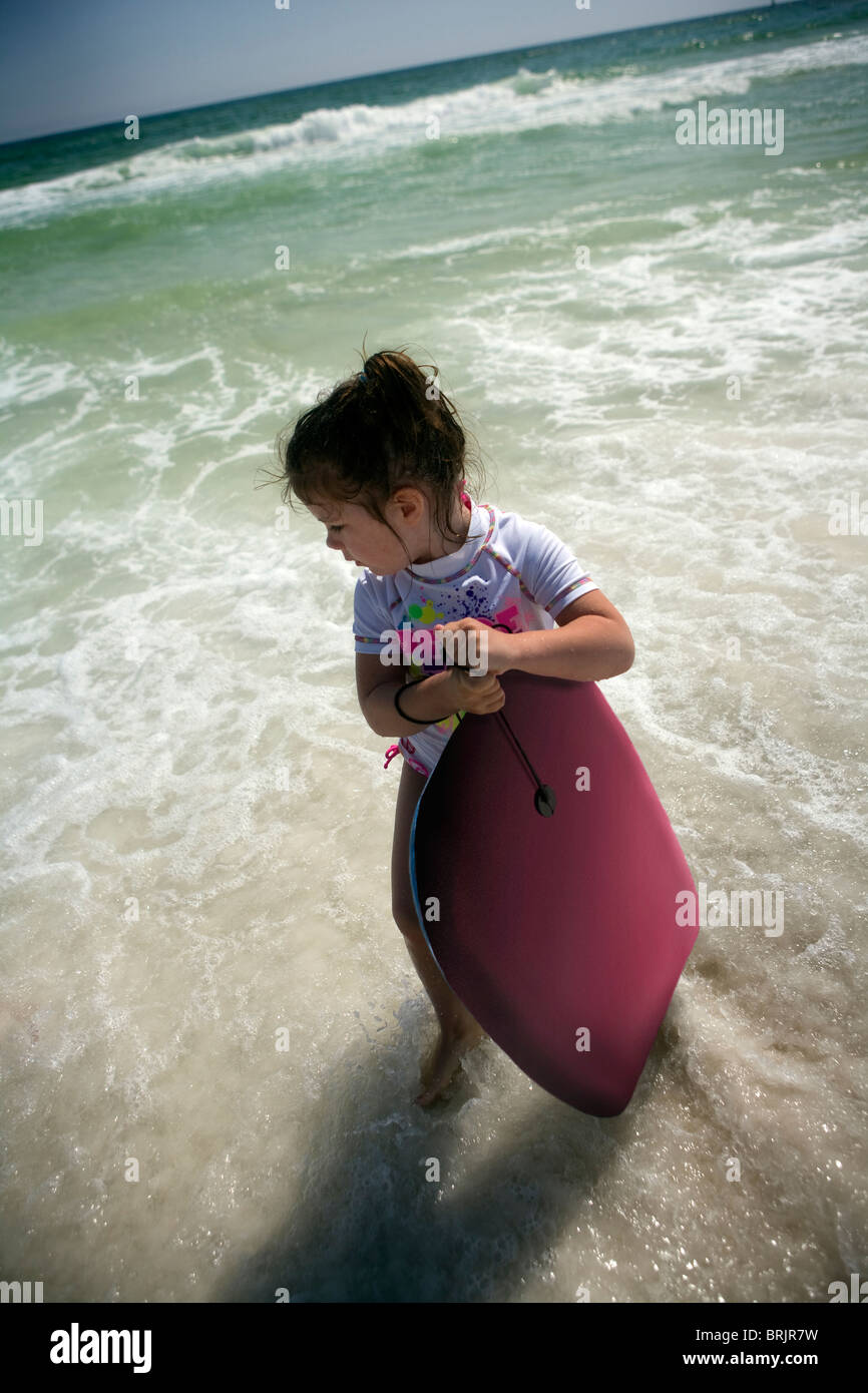 A little girl is holding a body board in the ocean near the shore. Stock Photo