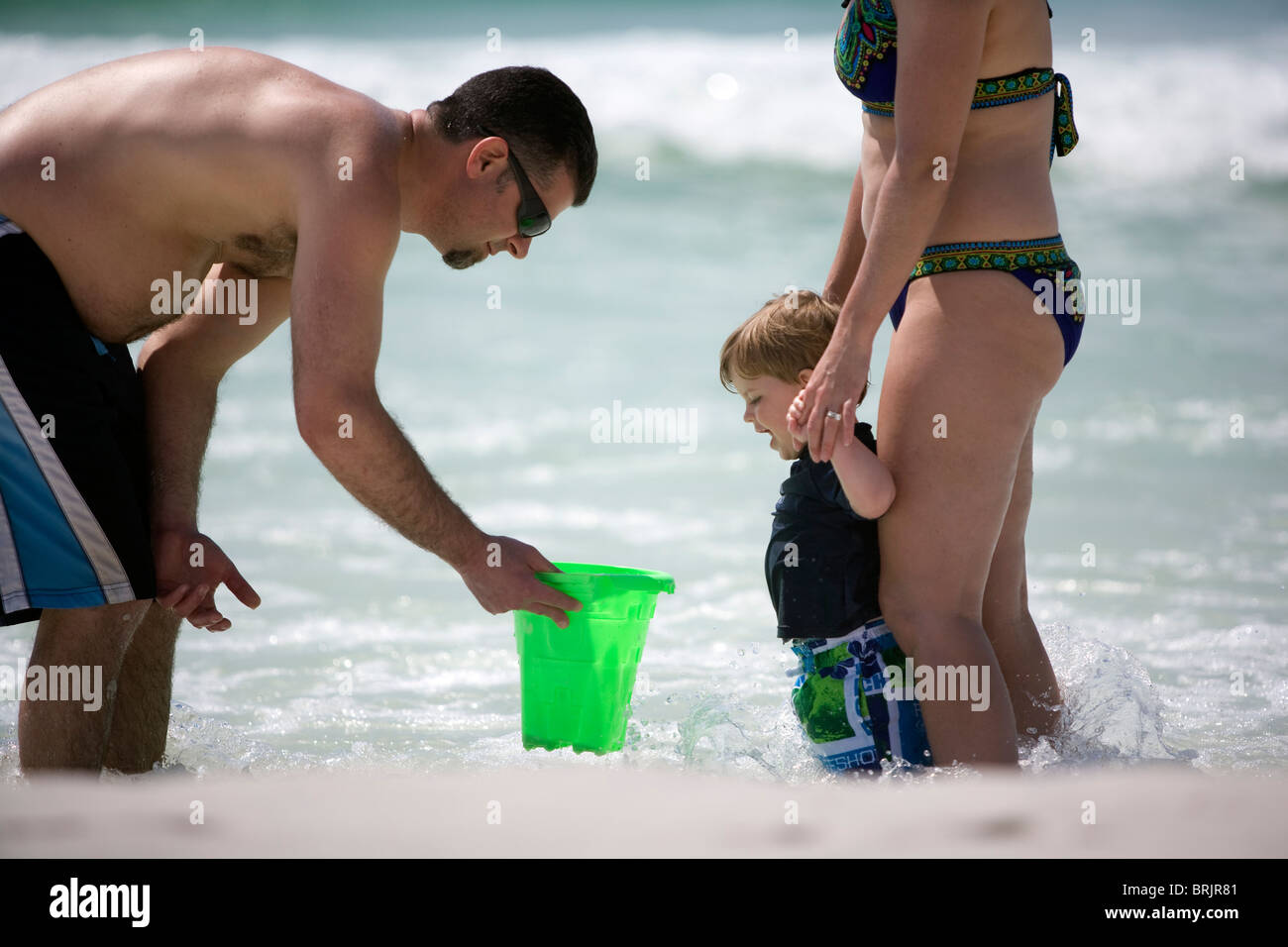 A father is showing a mother and son what's in a bucket at the shoreline. Stock Photo