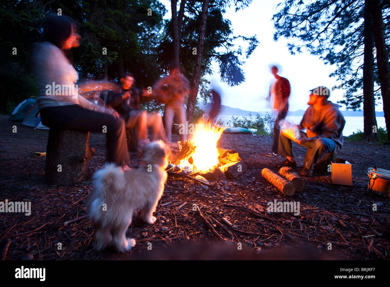Young adults camping sit around a fire next to a lake in Idaho. Stock Photo