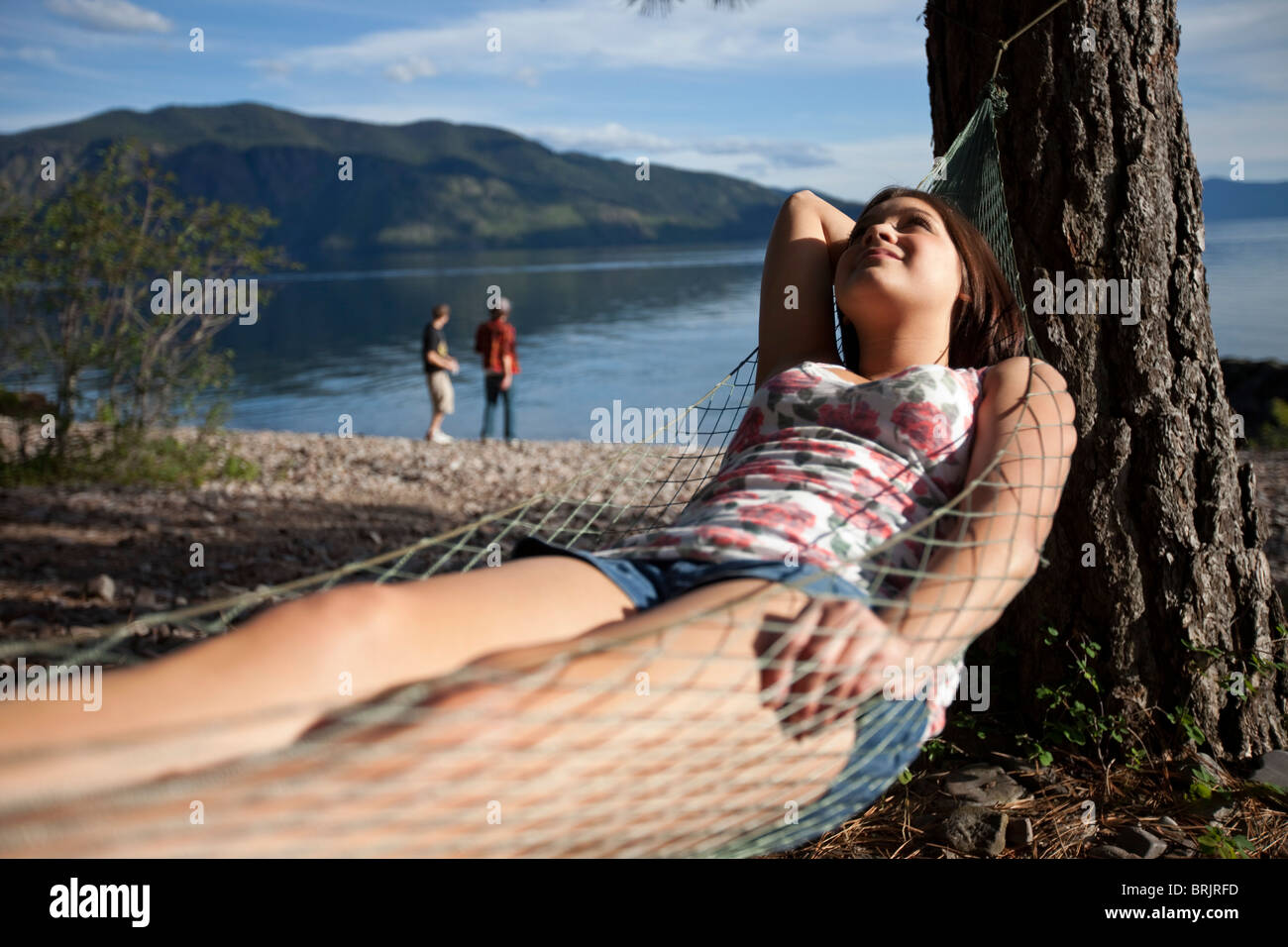 A women relaxes in a hammock with her friends skipping rocks on a lake in Idaho. Stock Photo