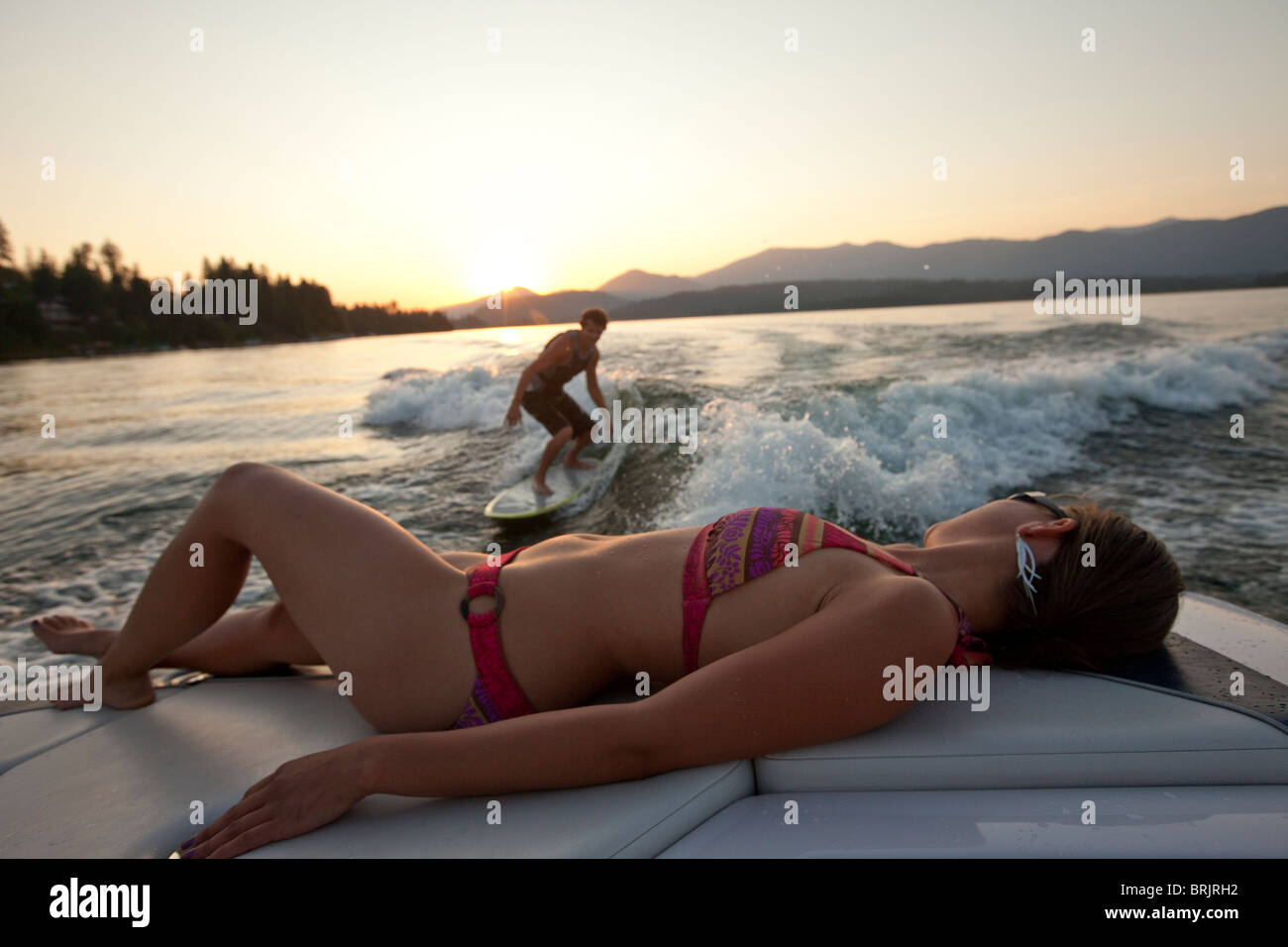 Young man wakesurfing in Idaho as a girl in a bikini watches from the boat. Stock Photo
