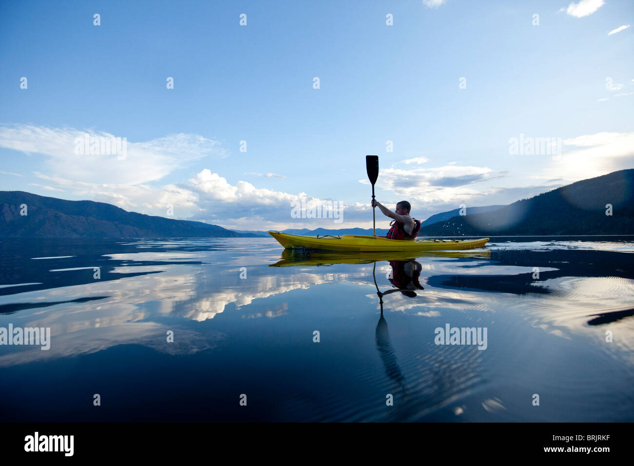 Young man paddles yellow kayak on lake. Stock Photo