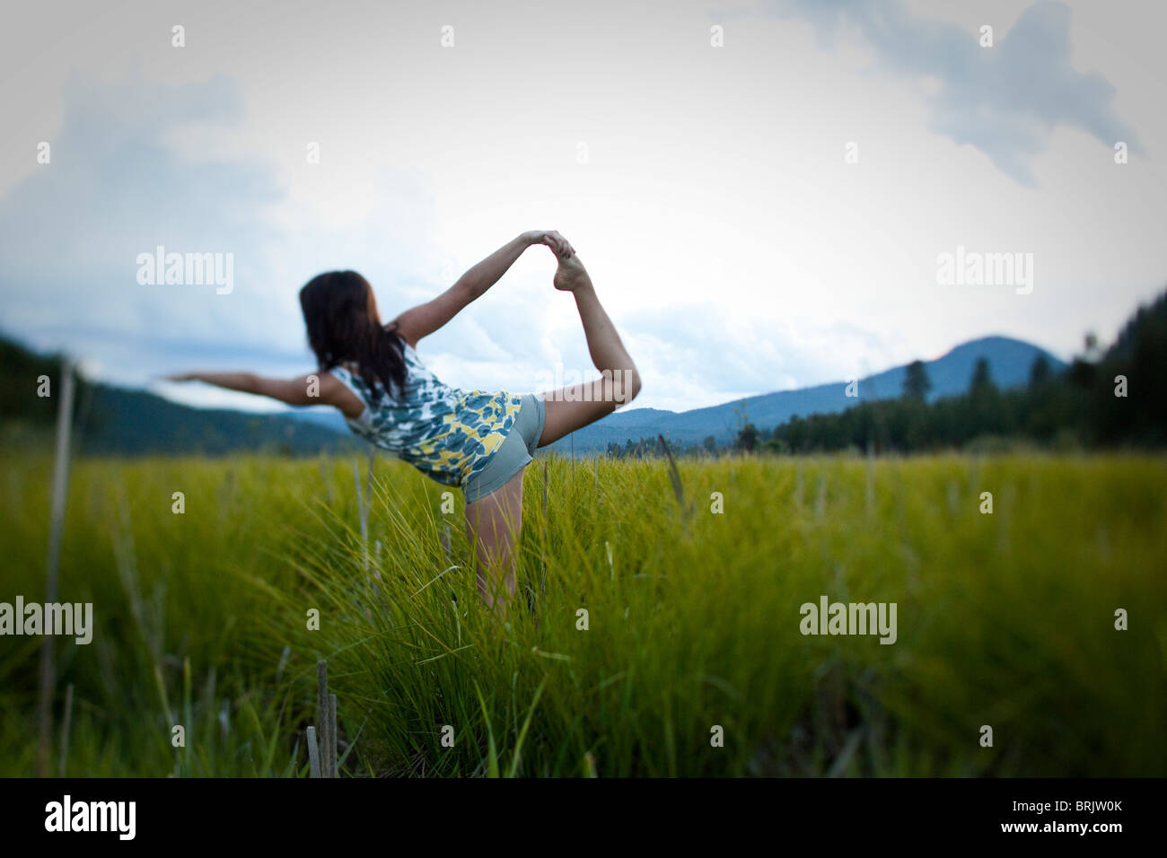 Young woman practices yoga in a grassy field. Stock Photo