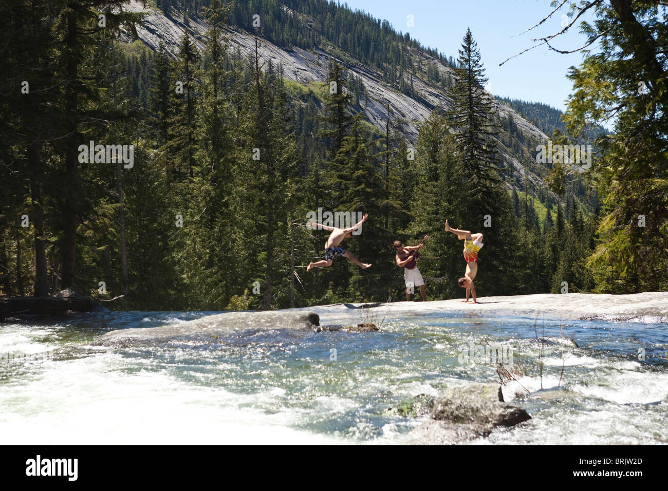 Three young men enjoy dancing and listening to the guitar next to a river in Idaho. Stock Photo