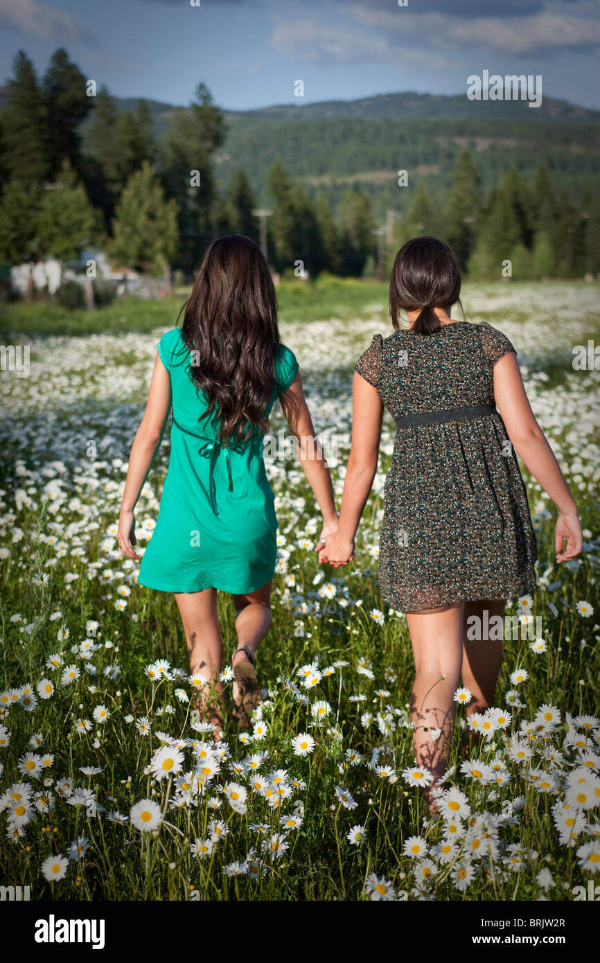 Two young women hold hands while walking through a field of wild flowers in Idaho. Stock Photo