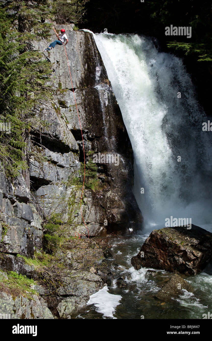 A young man rappels down a cliff next to a waterfall in Idaho. Stock Photo