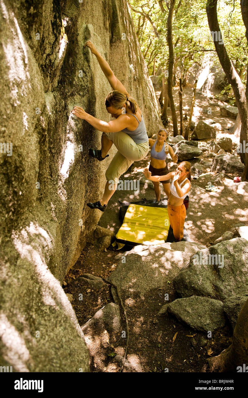 Protected by her friends spotting below, a woman boulders in Utah's Wasatch Mountains. Stock Photo