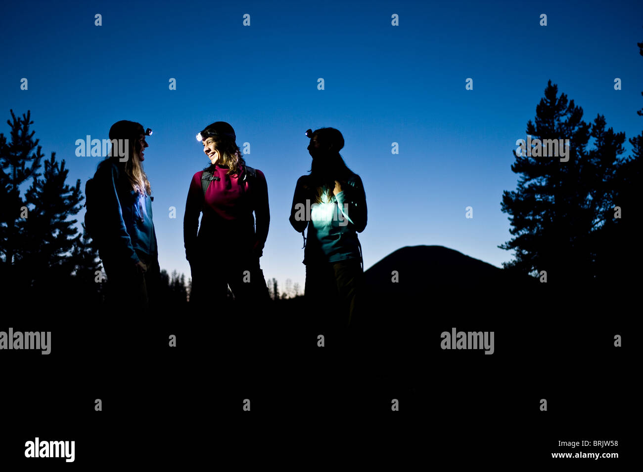 Three women talk while enjoying a twilight hike illuminated by headlamp. Stock Photo
