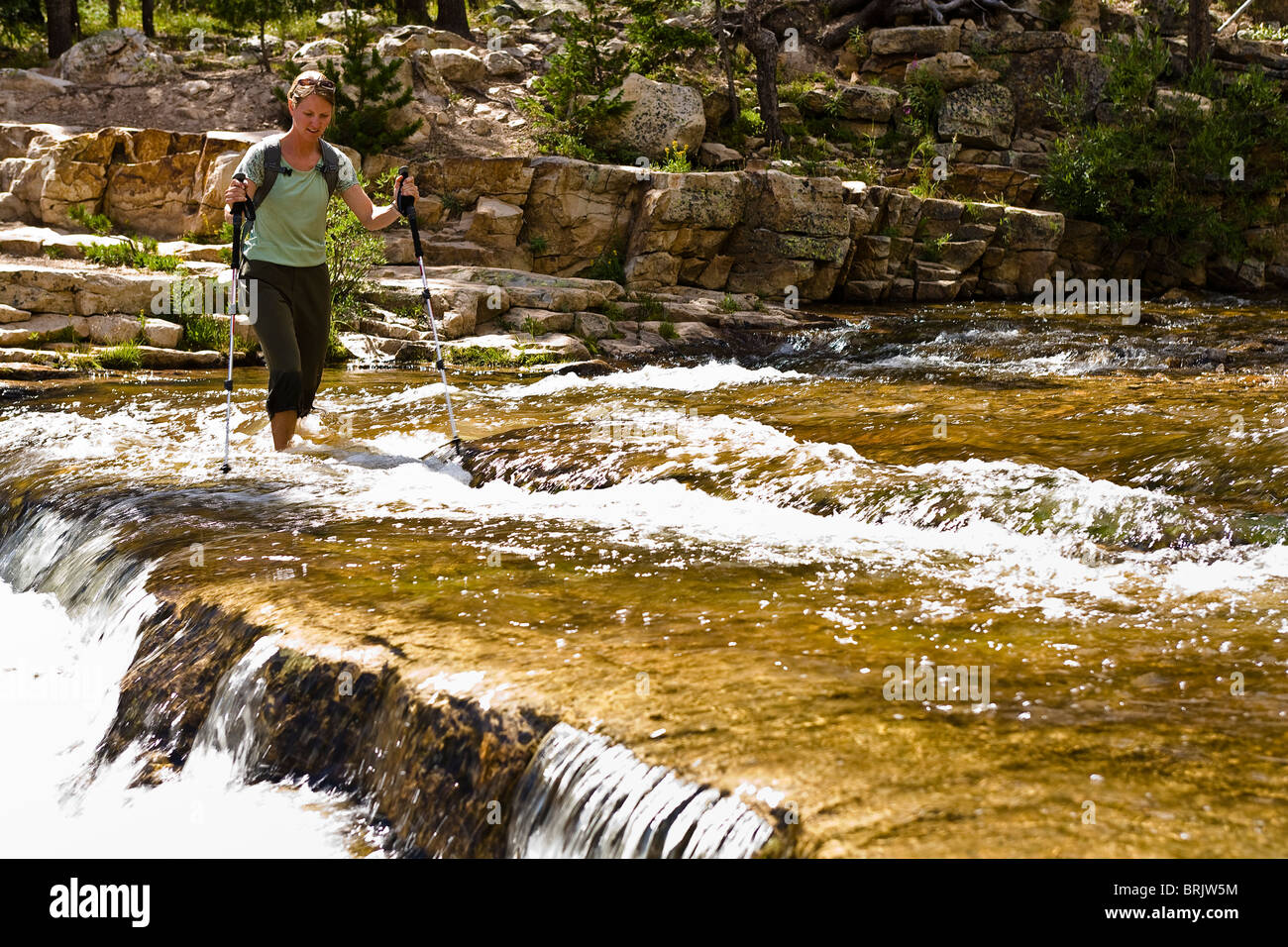 A woman wades across the Provo River in Utah's Uinta Mountains. Stock Photo