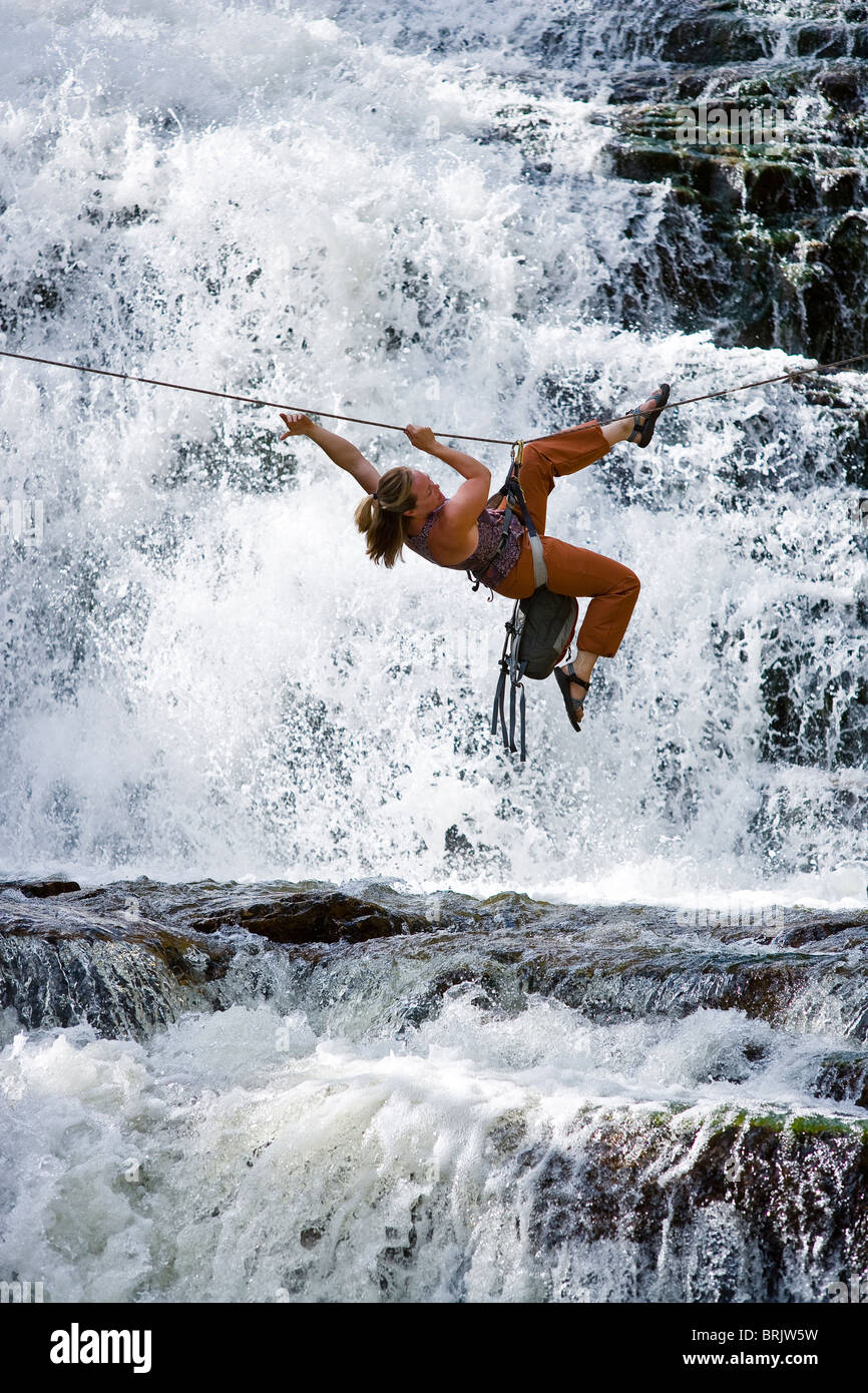A woman crosses a waterfall using a Tyrolean Traverse on a rope. Stock Photo