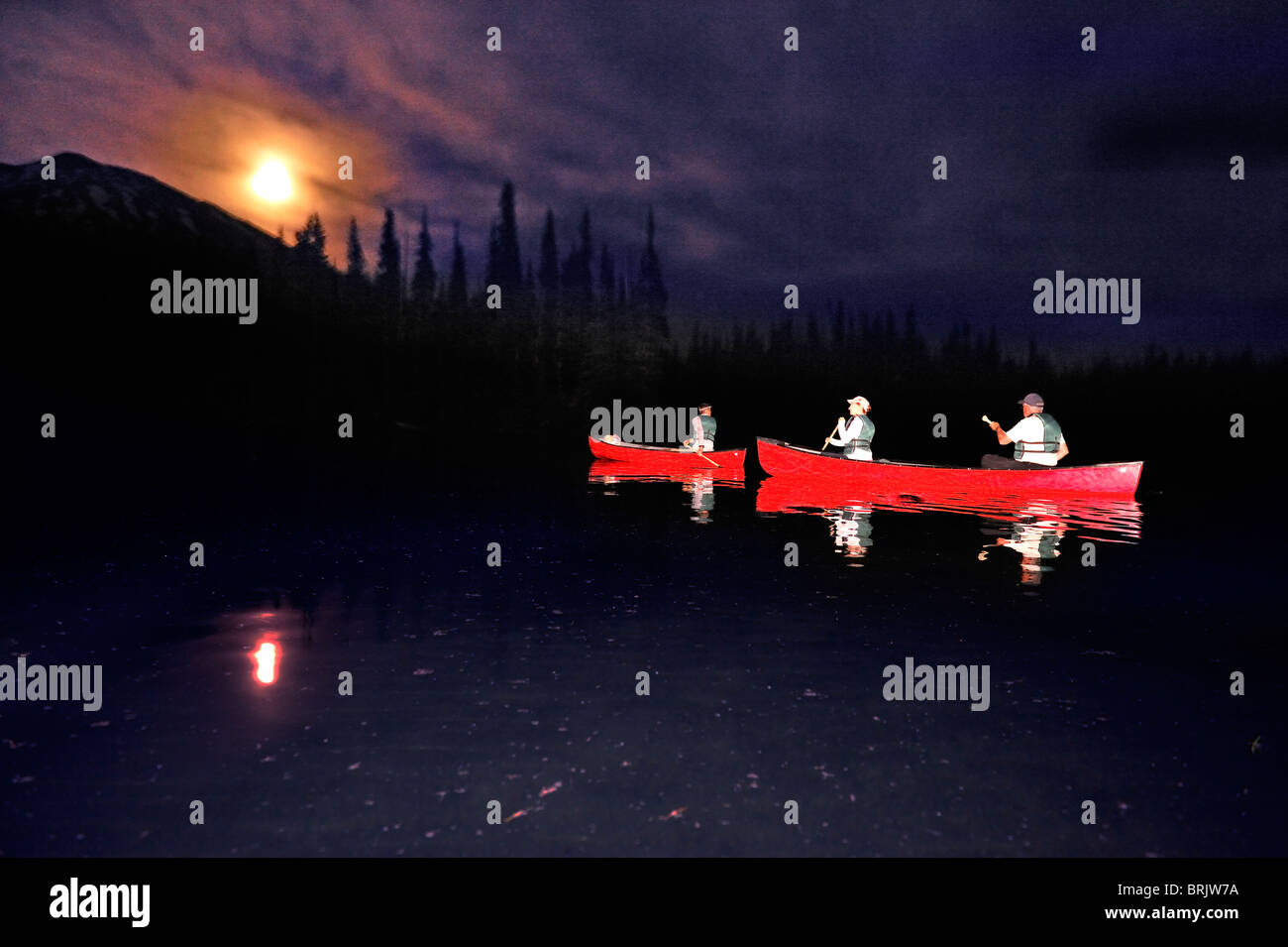 A group canoeing in a red boats at night on a mountain lake in Oregon