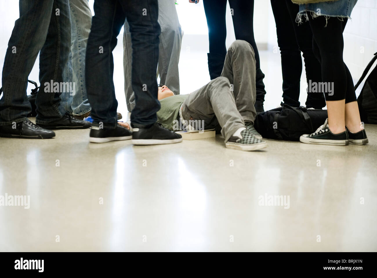 Bullies surrounding and threatening teenage boy lying on floor Stock Photo
