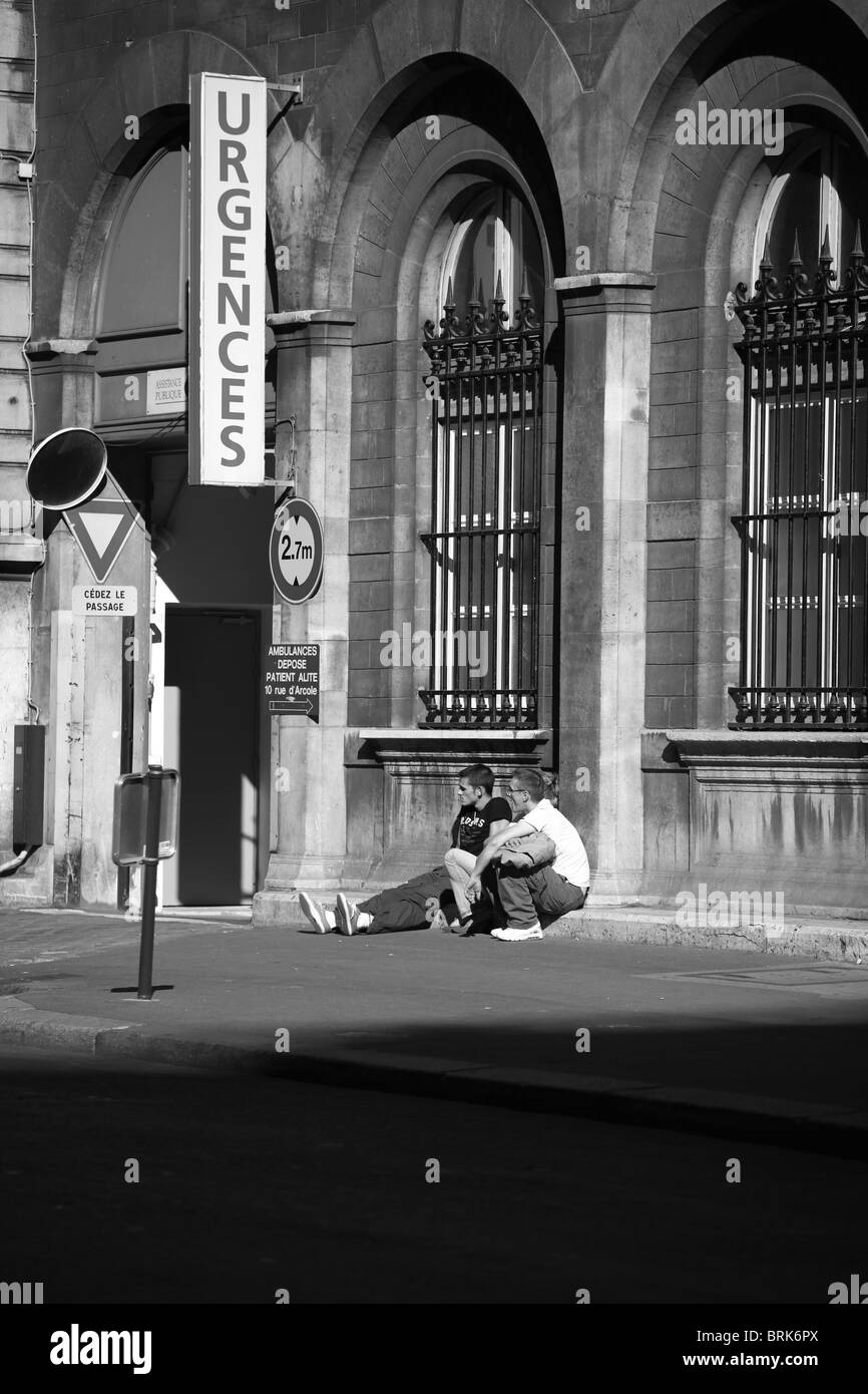 Two men sitting on pavement in Paris near the entrance of the Emergency