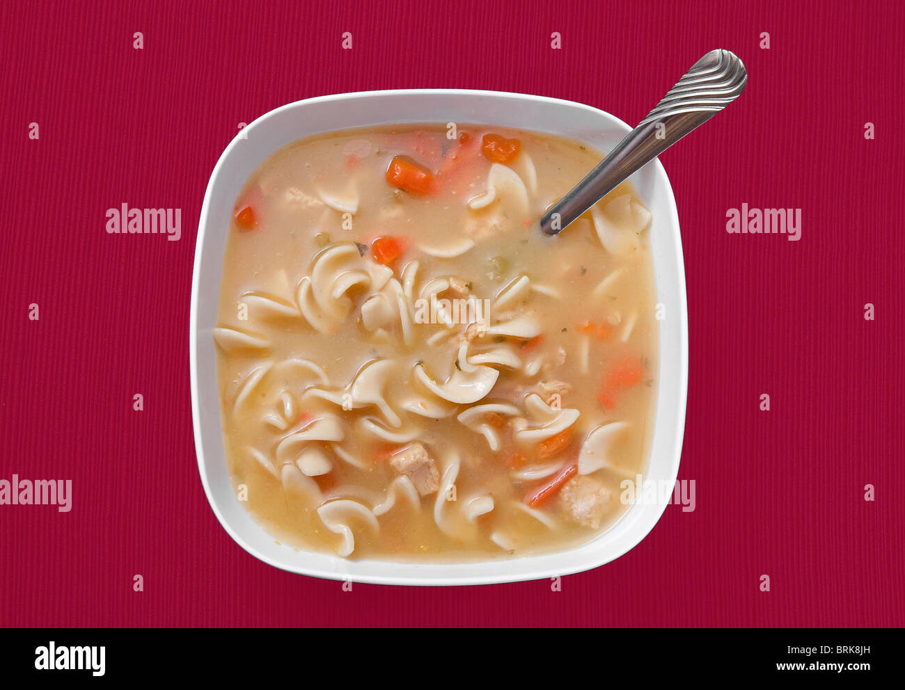 one large bowl of chicken noodle soup in a white bowl over a red