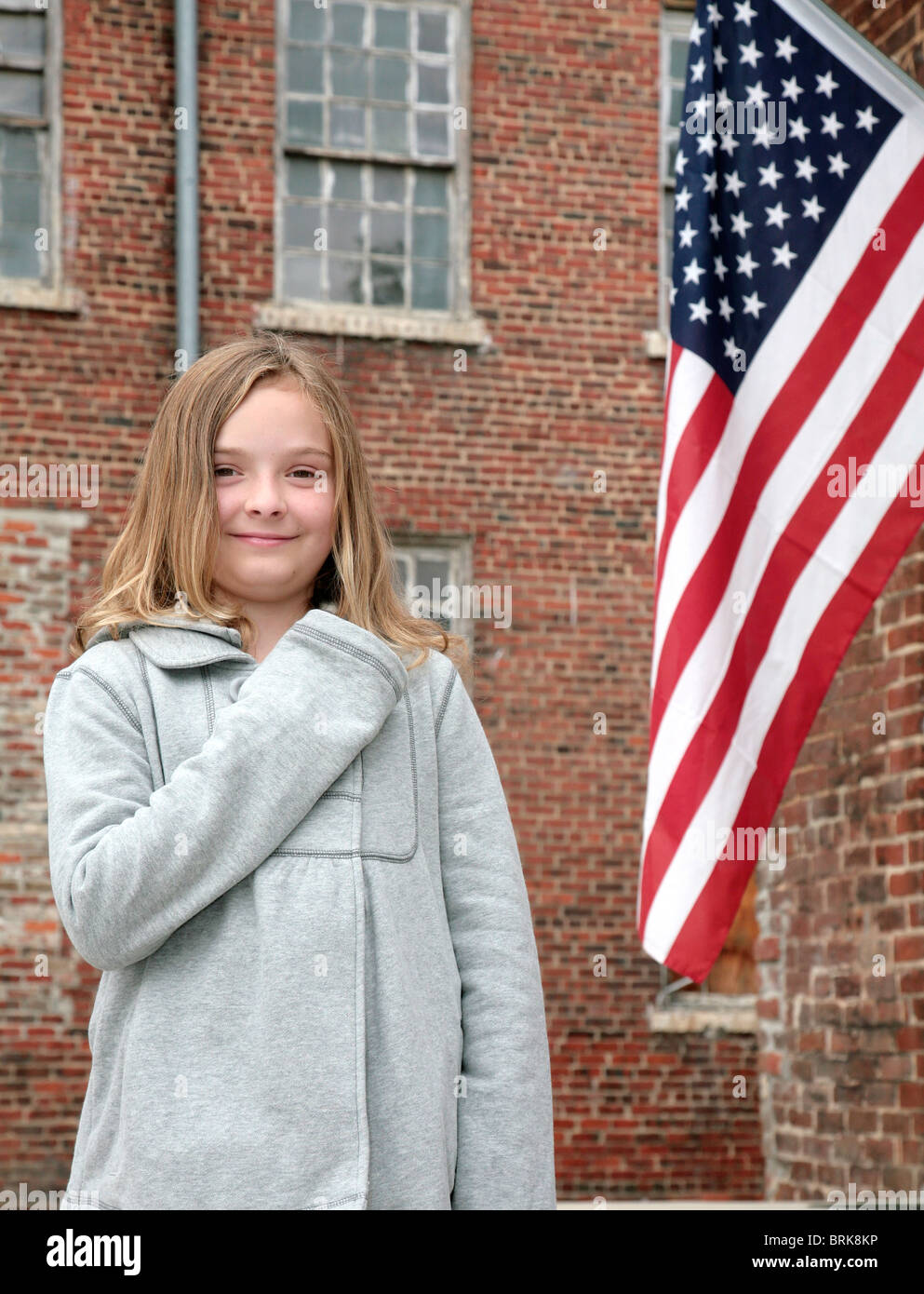 one young cute child with hand on her heart near an American Flag outdoors Stock Photo