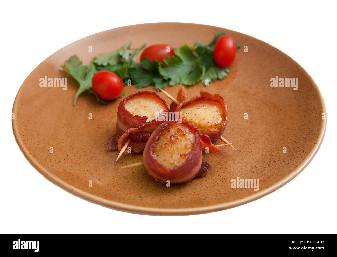 plate of three bacon wrapped scallops with cherry tomato garnish on a brown plate isolated on white Stock Photo