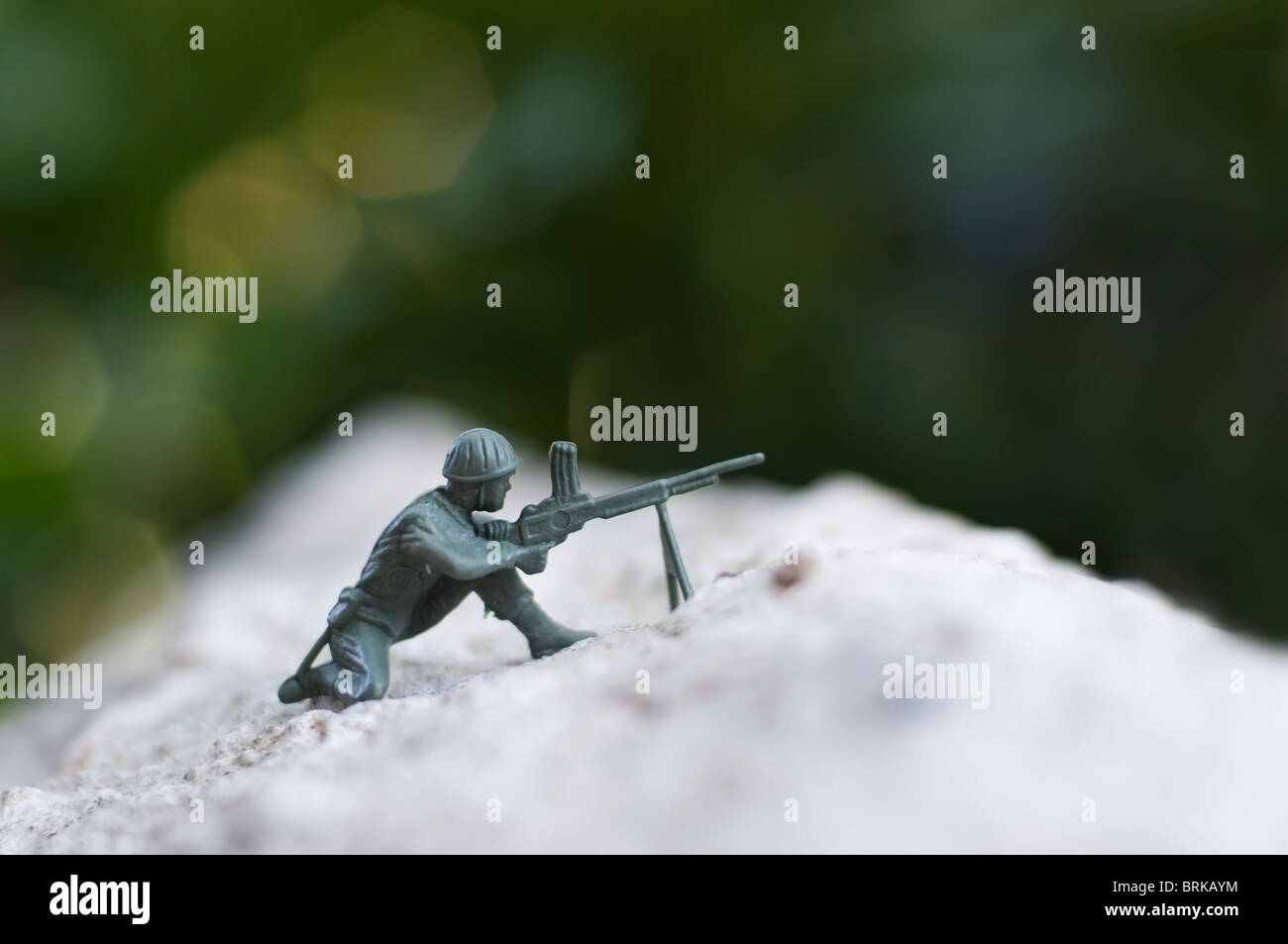 A green plastic toy soldier takes aim with his weapon in the rugged outdoors. Stock Photo