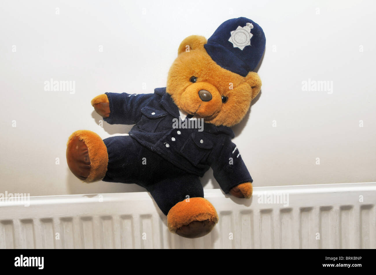 A teddy bear dressed as a policeman sitting awry on a central heating radiator. Stock Photo