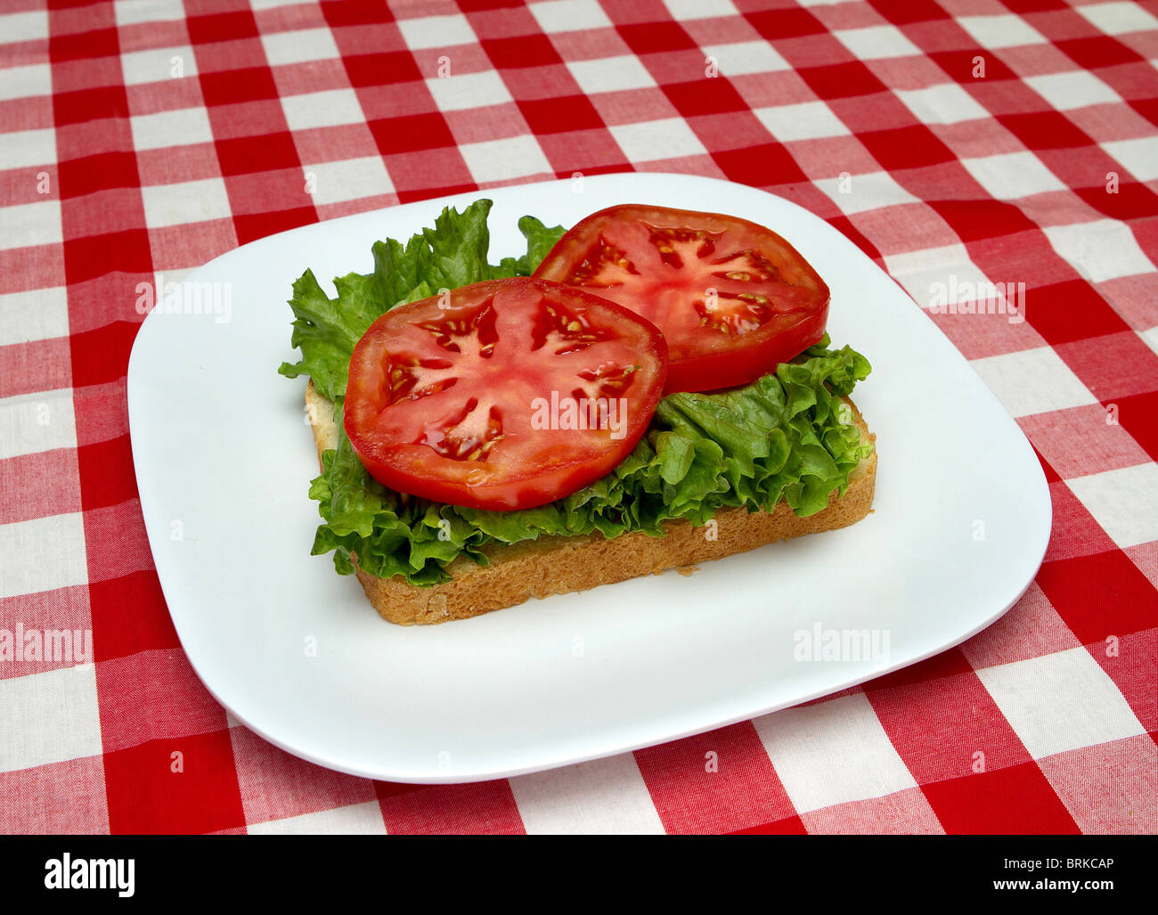 incomplete blt sandwich on a white plate with red checked background Stock Photo