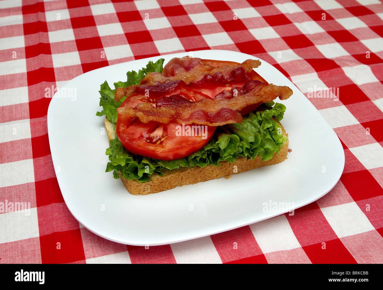 incomplete blt sandwich on a white plate with red checked background Stock Photo