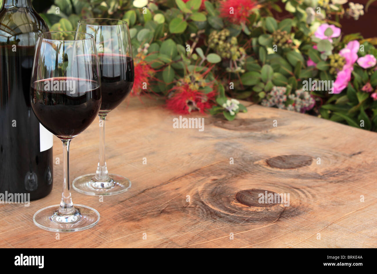 Bottle & Glasses of Red Wine on Outdoor  Wooden Table with Pohutukawa Stock Photo